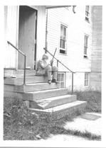 SA0081 - Elder William Anderson was from the South Family. He is shown sitting on the steps of an unidentified building, holding a long stick. Identified on the reverse.